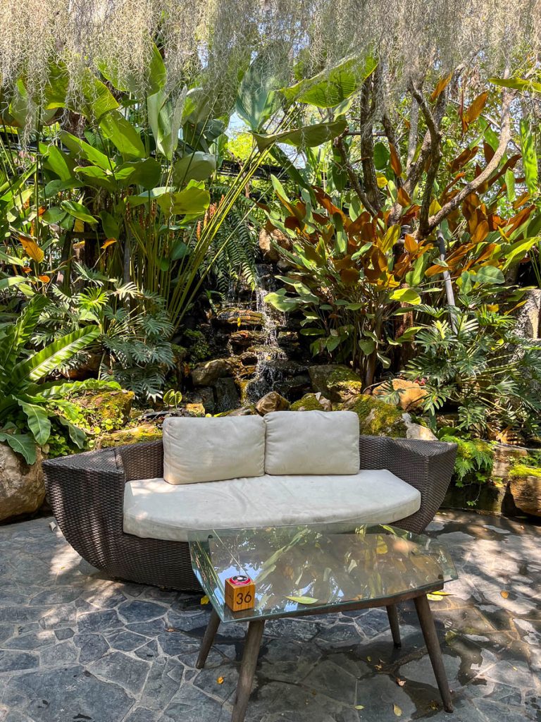 Tranquil sounds and stylish comfort—A sculptural wicker lounger by a calming waterfall at Caramellow