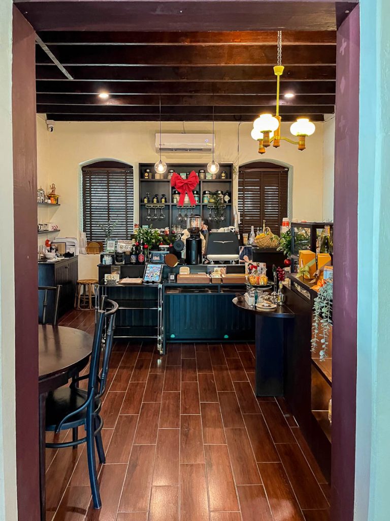 View through an archway into The Pantry counter area at Baan 104, with dark wooden cabinetry, pendant lights, and pastries on display