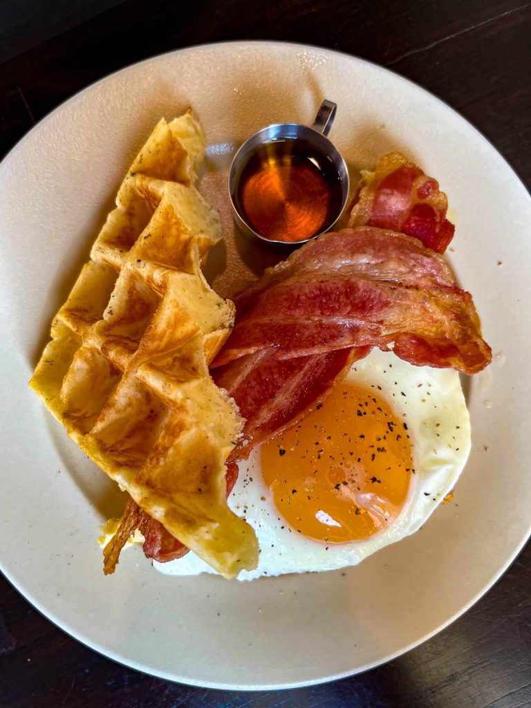 Plate with crispy waffle, sunny-side-up egg, bacon, and maple syrup at The Pantry in Baan 104, Chiang Mai