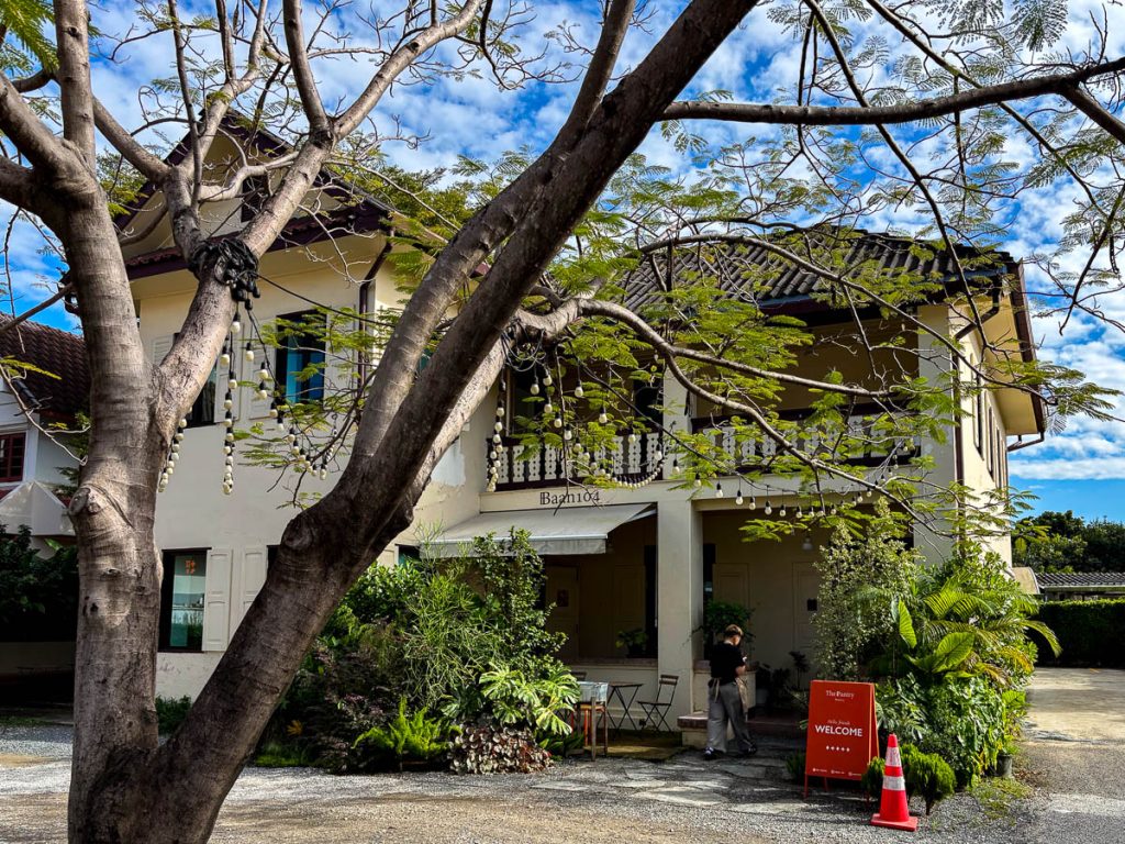 An exterior shot of Baan 104 showing its colonial-style facade, beneath the shade of a flame tree