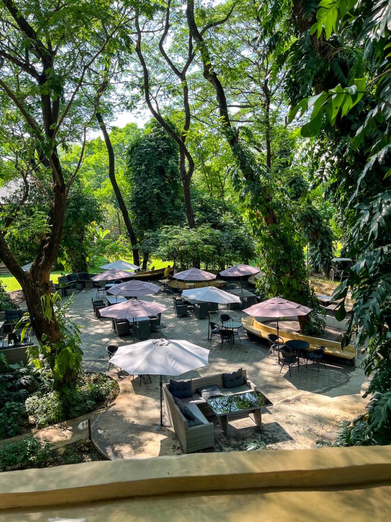 Outdoor garden seating at Much Room Cafe Chiang Mai with umbrellas and sofas under the trees