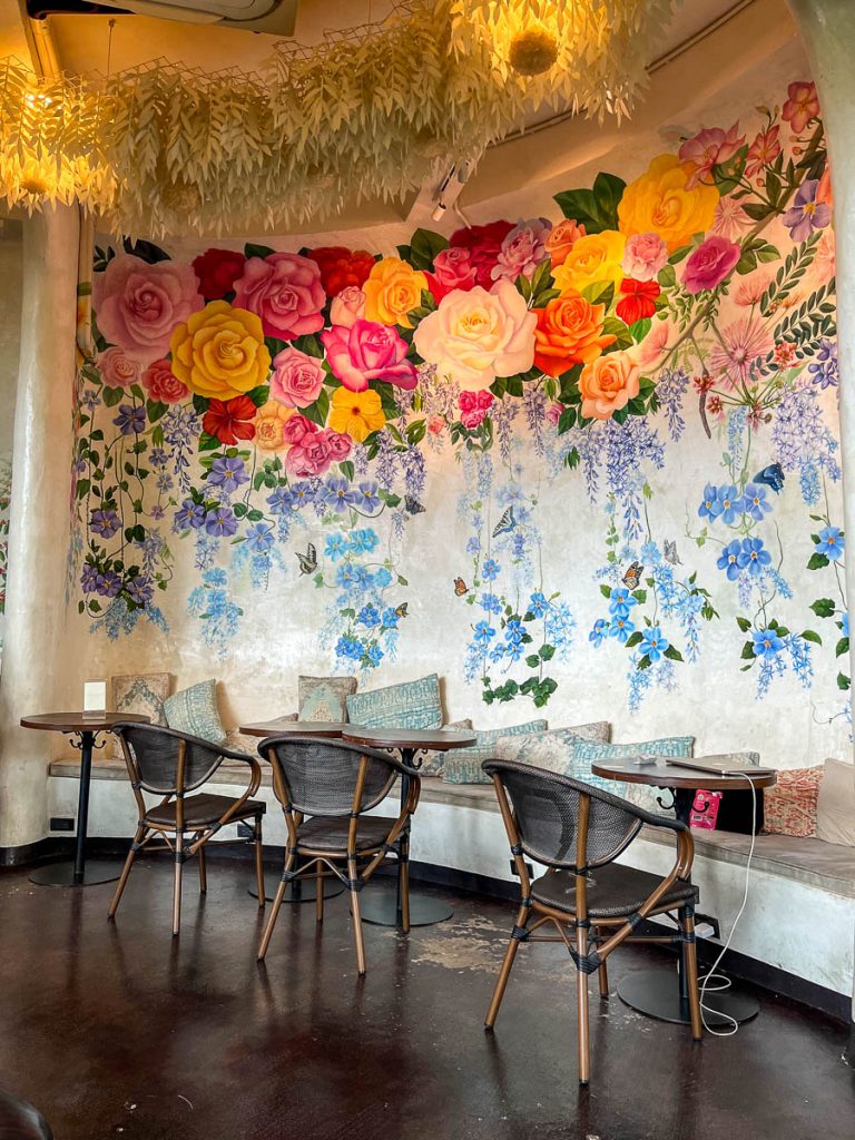 Interior of Much Room Cafe Chiang Mai with colourful floral mural and cafe seating
