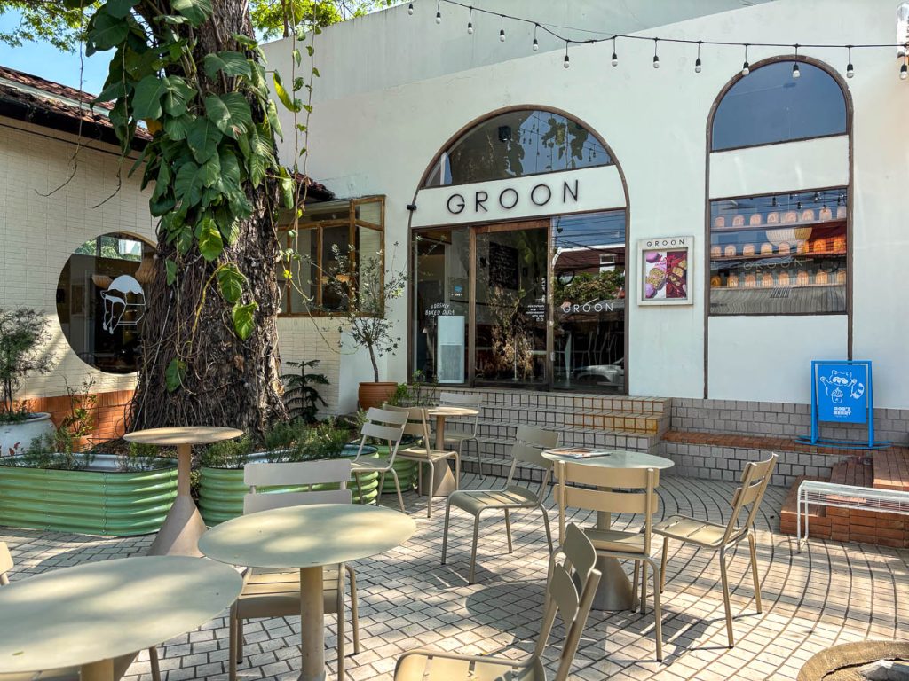 Exterior of GROON Bread & Brunch Cafe in Nimman, Chiang Mai, featuring a leafy courtyard, arched windows, and Mediterranean-inspired design